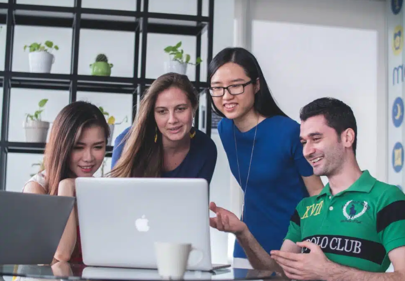 Four people collaborating over a laptop in an office setting.