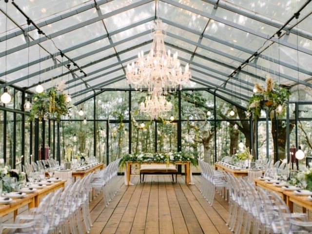 Indoor dining setup in a glasshouse with wooden tables and greenery
