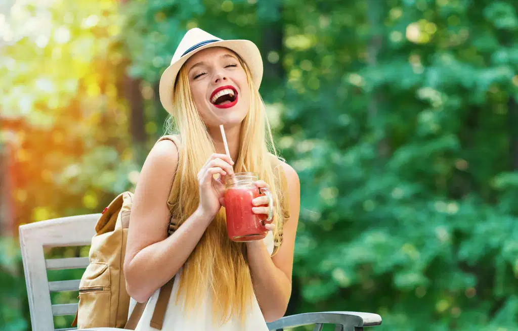 Smiling woman in a hat holding a drink outdoors