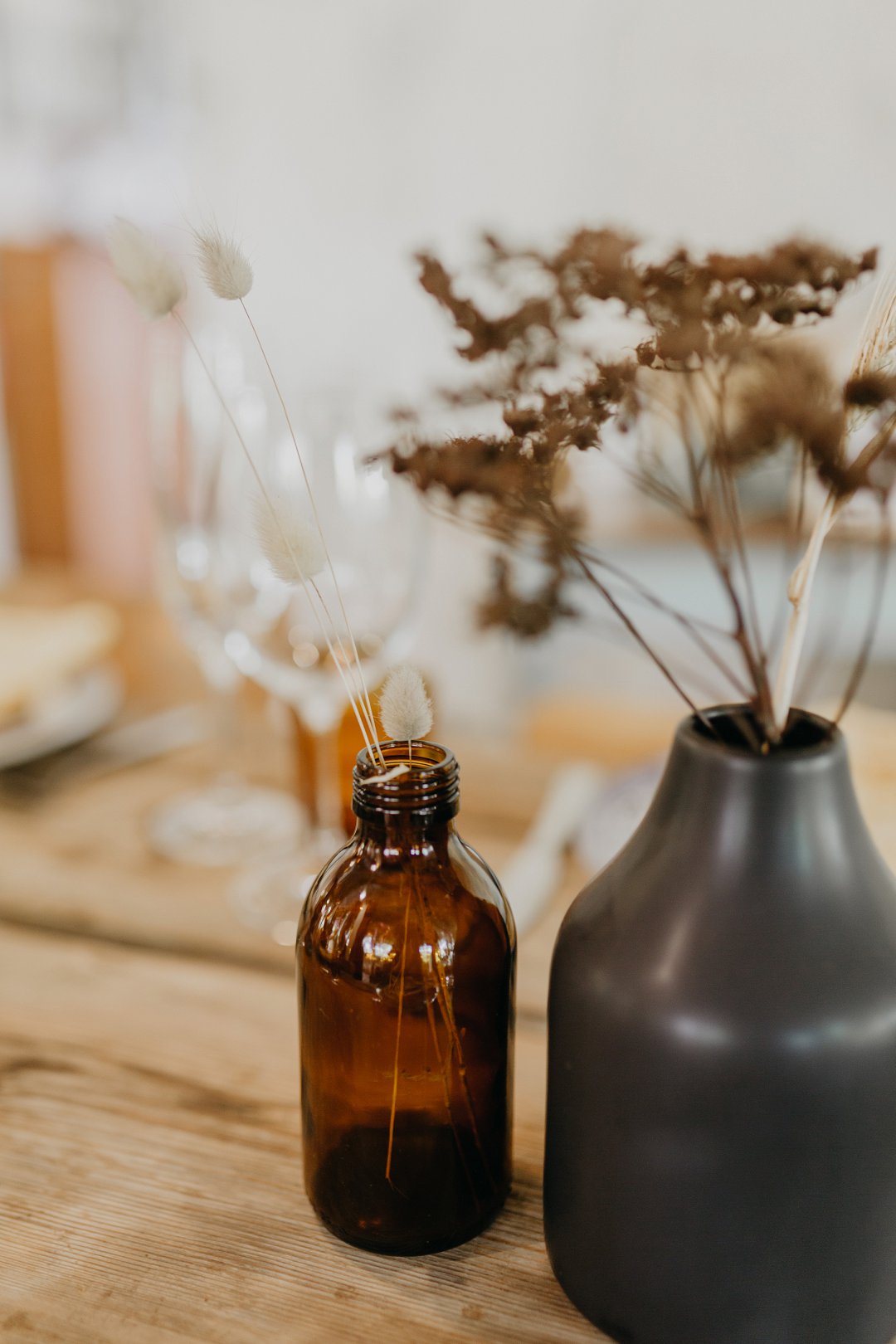 Dried flowers in brown and black bottles on a wooden table
