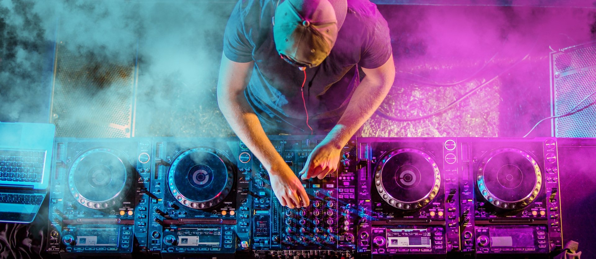 DJ operating equipment with colorful lights and smoke effects.
