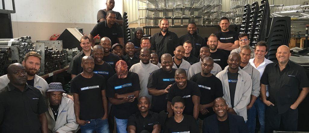A diverse team posed in a warehouse with staging equipment.