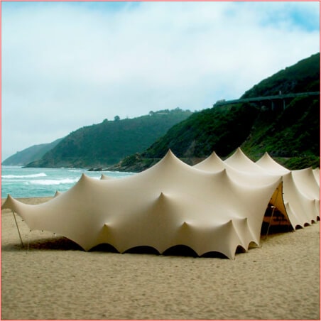 Large stretch tent set up on a beach near hills and a highway