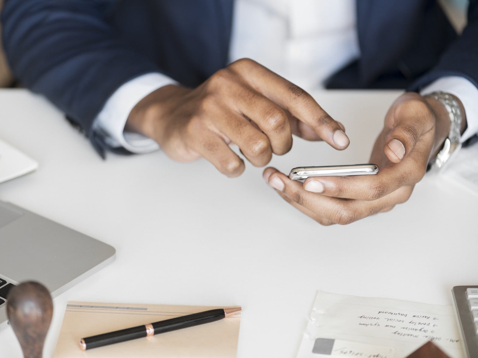 Person using smartphone at a desk with laptop and papers.