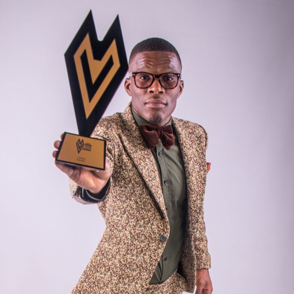 Comedian in a patterned suit holding a trophy.