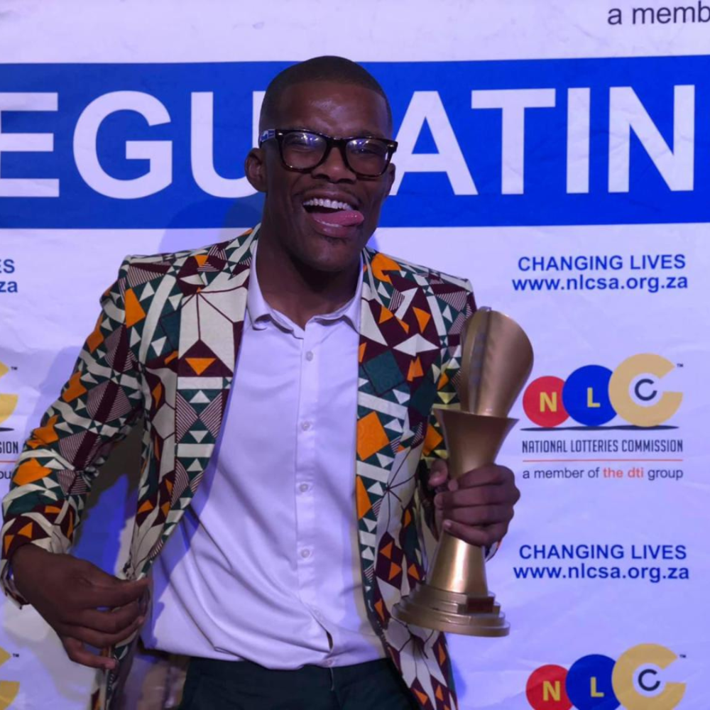 Comedian in patterned blazer holding a trophy