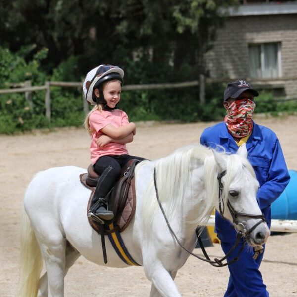 A child rides a pony with an instructor guiding alongside