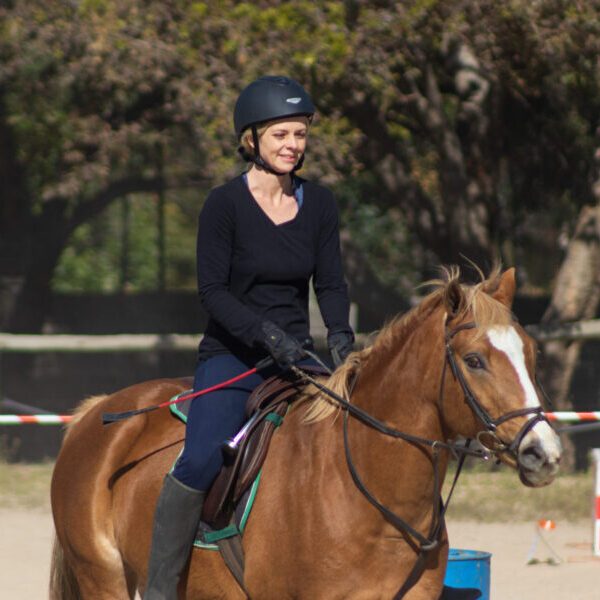 Adult rider on a brown pony in an outdoor arena.