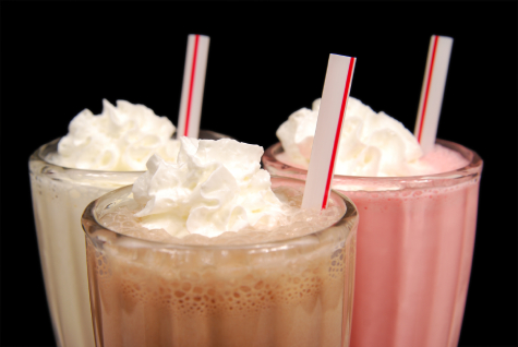 Three milkshakes in glasses with whipped cream and straws