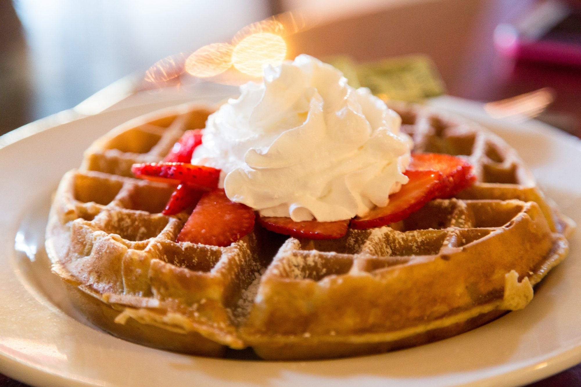 Plate of waffle topped with strawberries and whipped cream