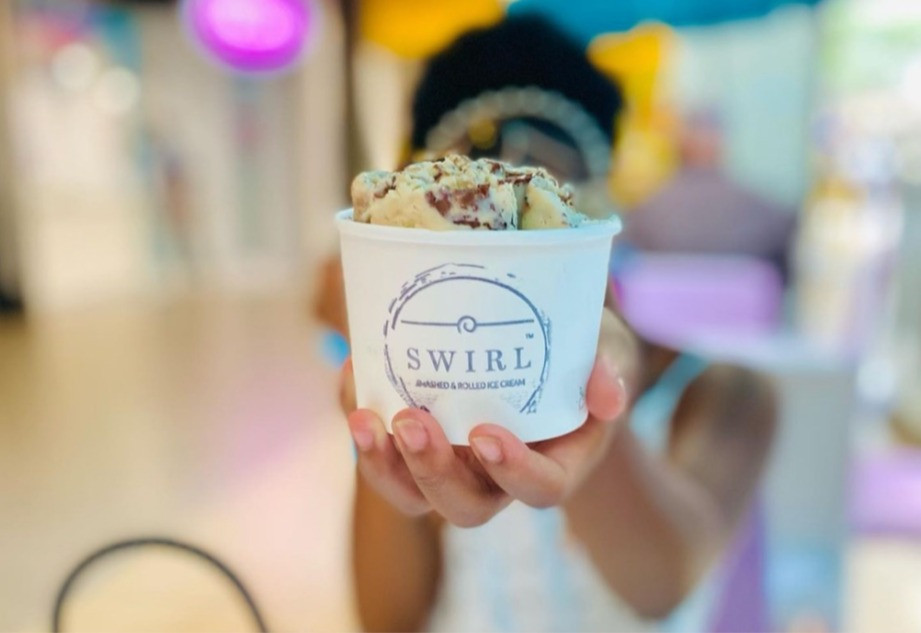 A hand holding a white ice cream cup with rolled ice cream inside.