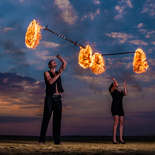 Two fire dancers performing with flaming staffs at sunset