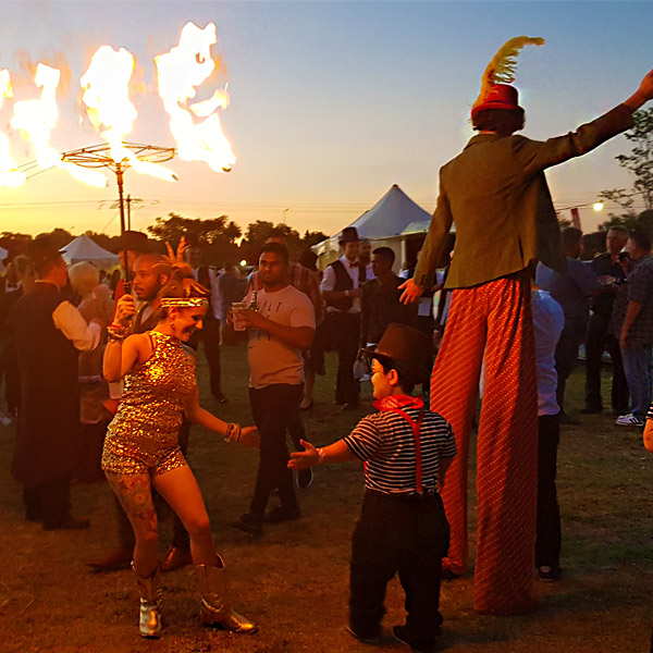 Fire dancers and stilt walkers performing at sunset