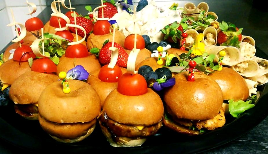 Platter of gourmet mini burgers with fresh toppings and colorful garnishes.