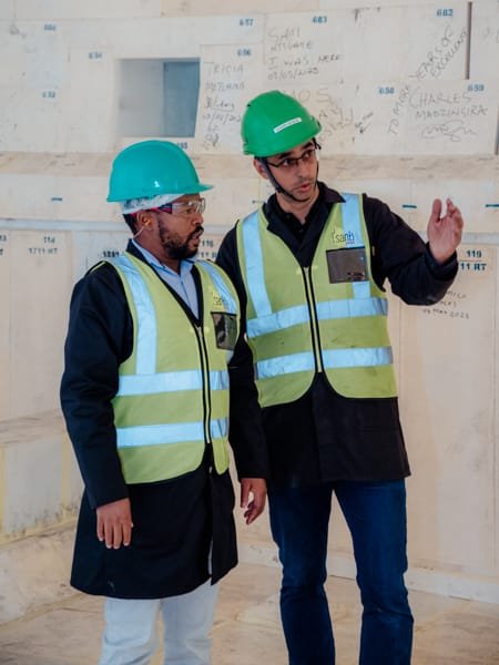 Two individuals in safety gear discussing a project indoors.