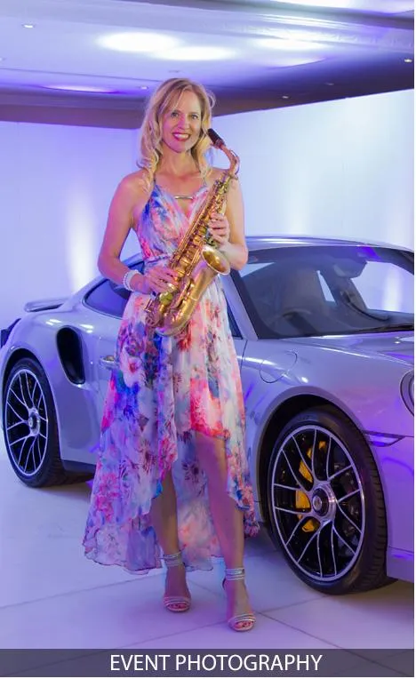 Female saxophonist posing with a luxury car