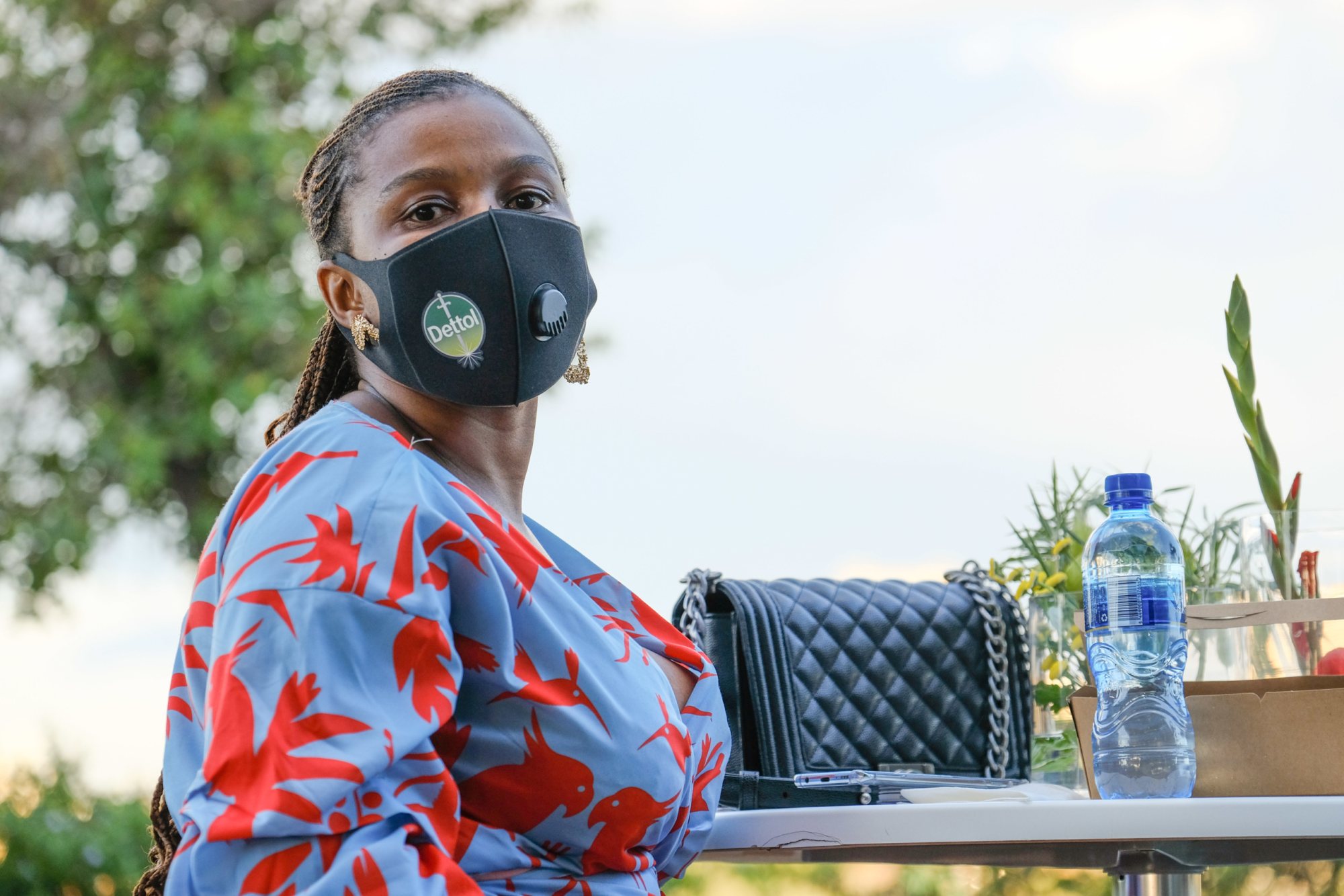 A masked guest seated at a table with water bottle and handbag