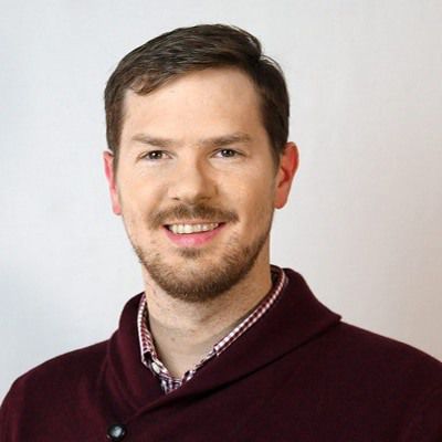 Professional headshot of a smiling man in a dark sweater.
