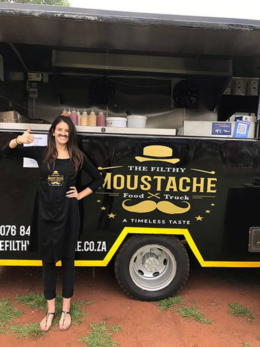 Staff member in apron next to The Filthy Moustache food truck