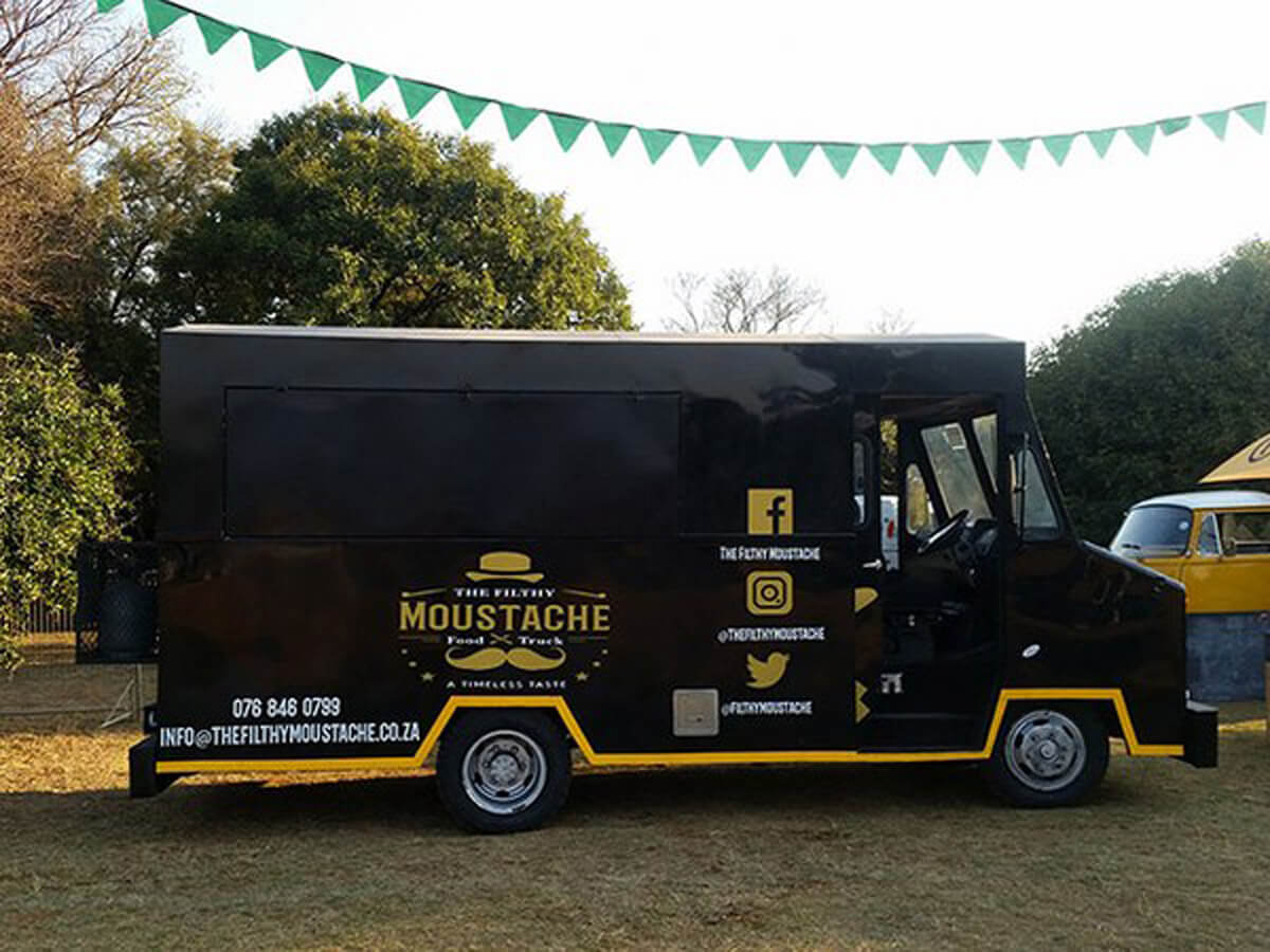 Black coffee truck with yellow accents and logo at an outdoor event.