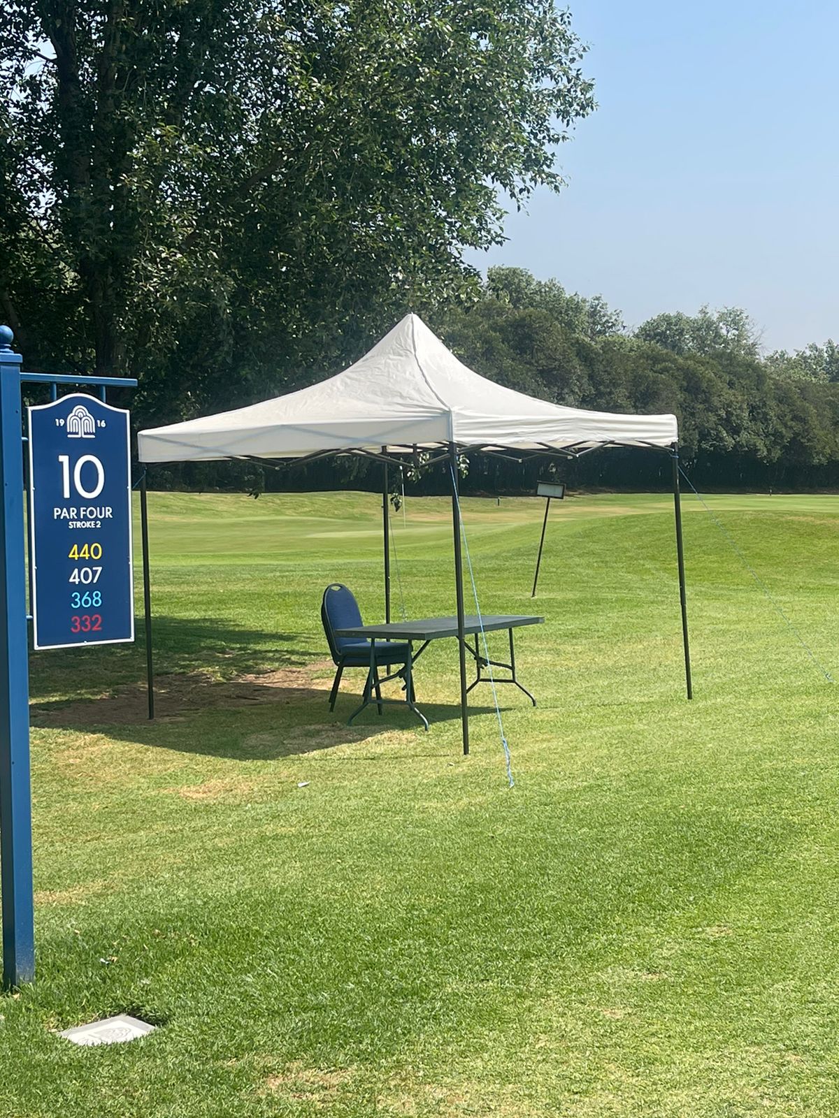 A gazebo set up on a golf course with a chair and table.