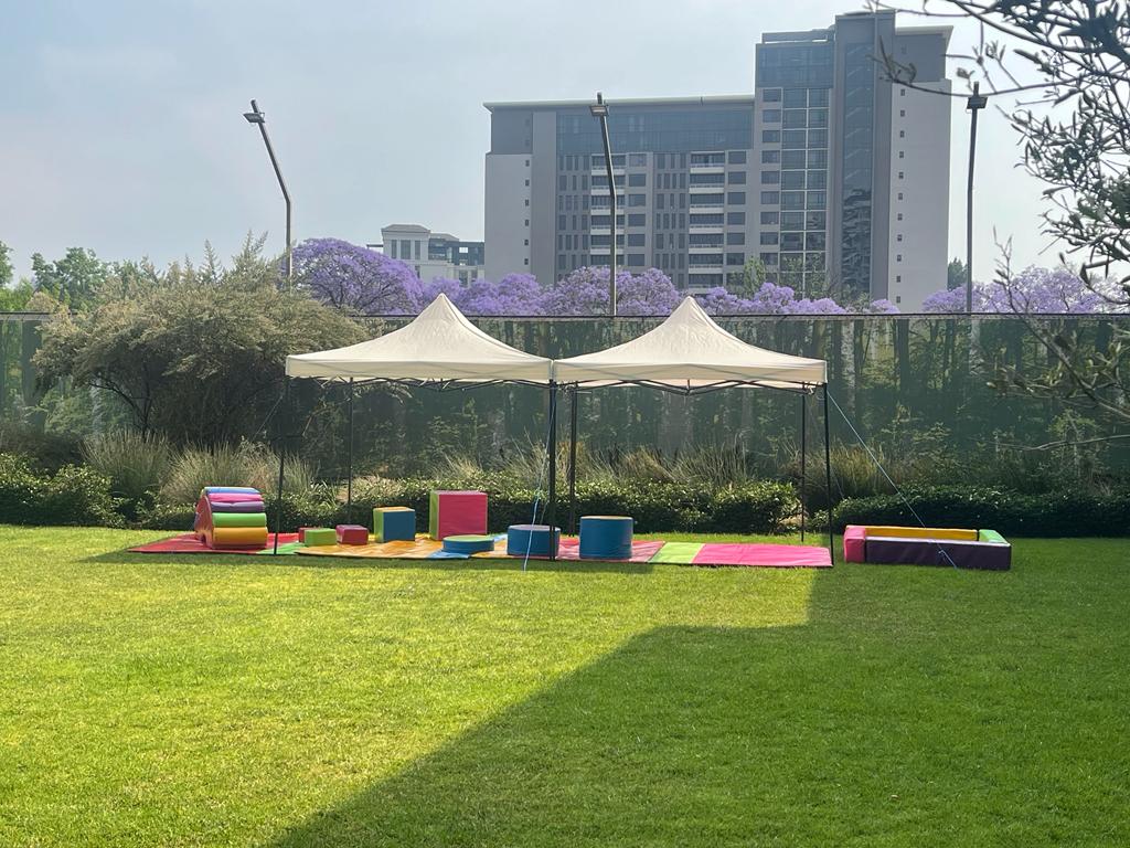 Gazebo setup with colorful play mats and equipment on a grass field.
