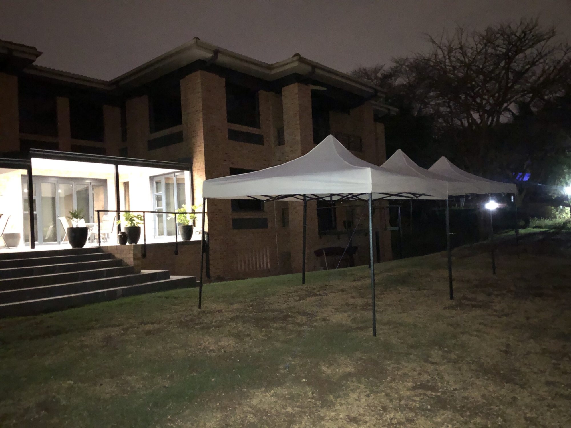 Three white gazebos set up in a garden near a building at night