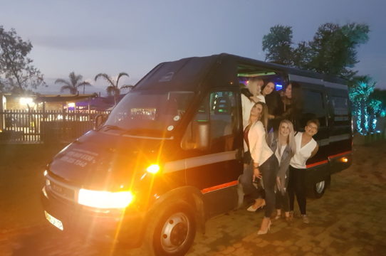 Group of friends posing by a Party Bus at dusk