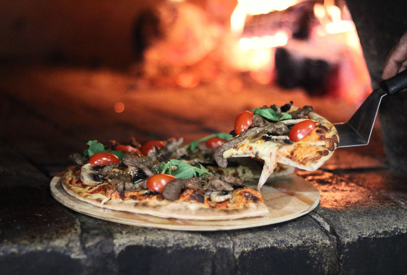 Wood-fired pizza being served with toppings and a rustic backdrop