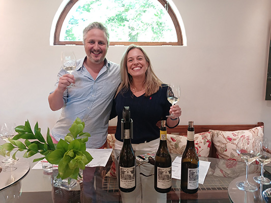 Two people holding wine glasses with bottles on the table.