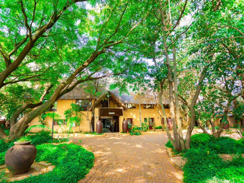 Lush entrance of The Garden Venue with greenery and rustic buildings.