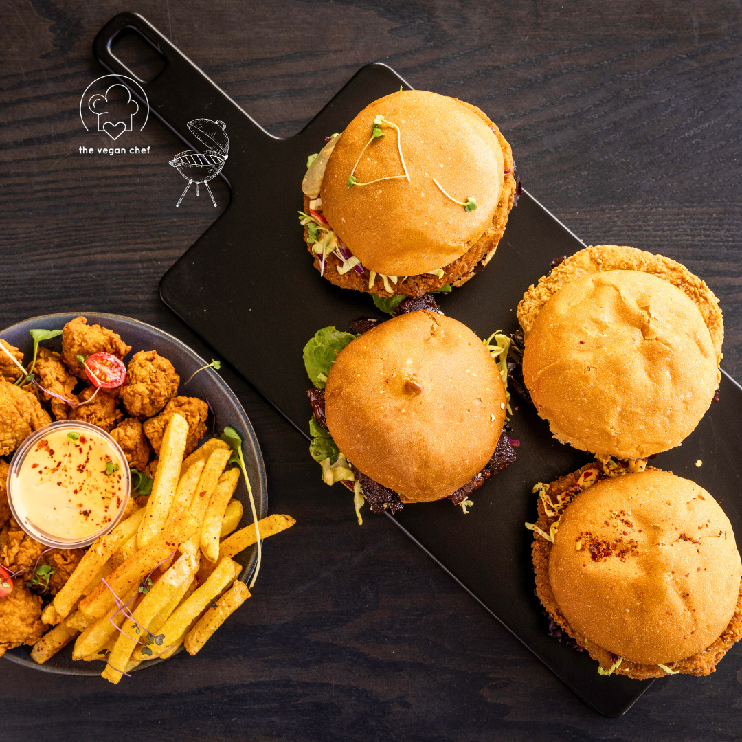 Four vegan burgers on a platter with fries and dipping sauce