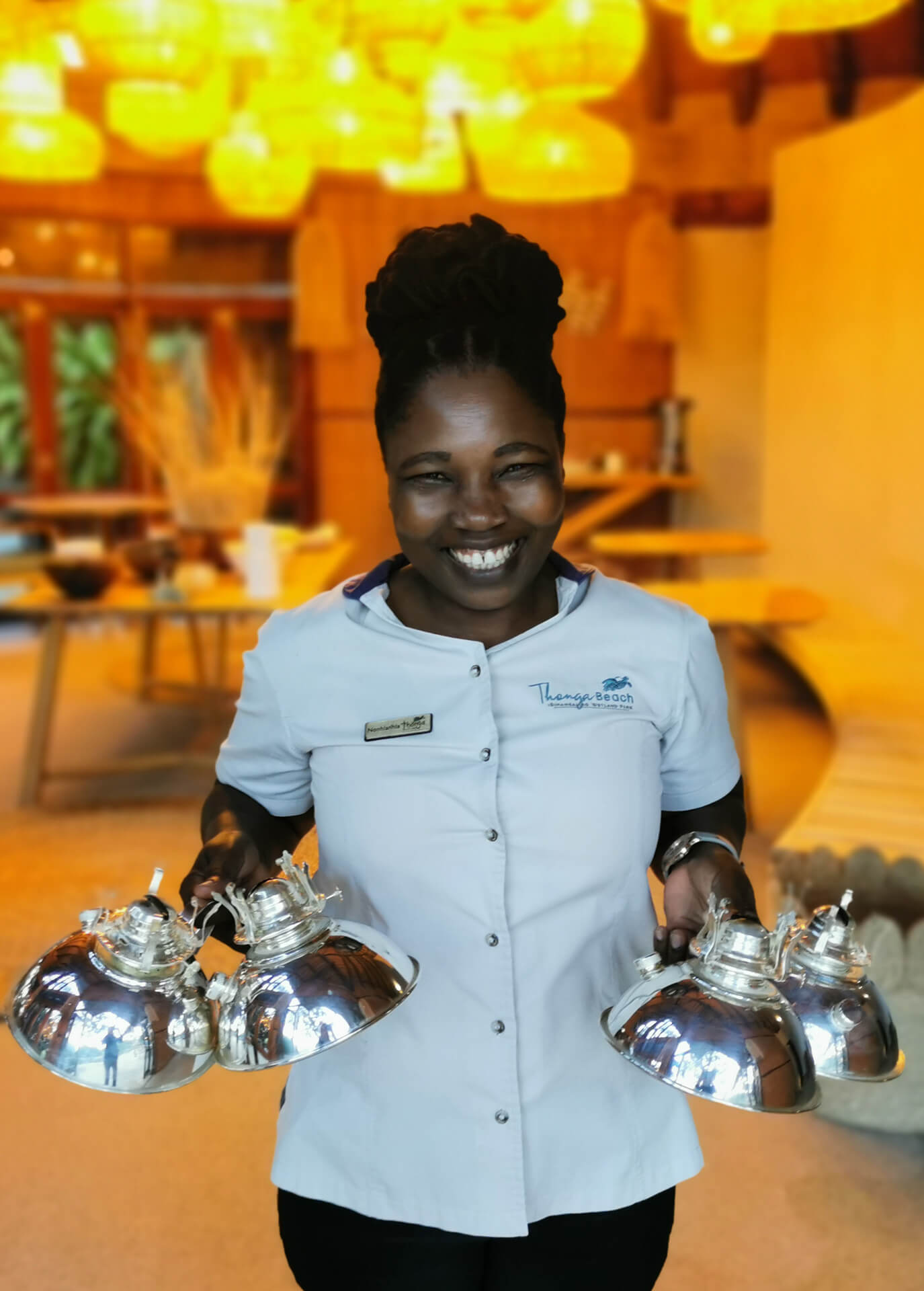 Staff member holding several serving cloches at Thonga Beach Lodge