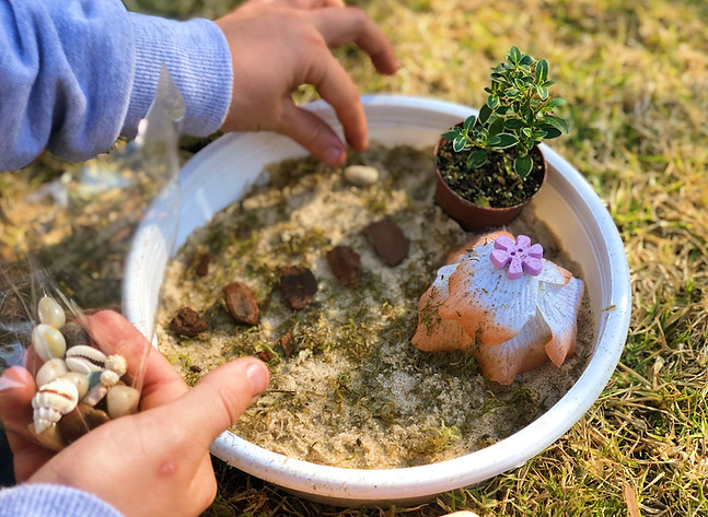 Child arranging sand art with shells and plants