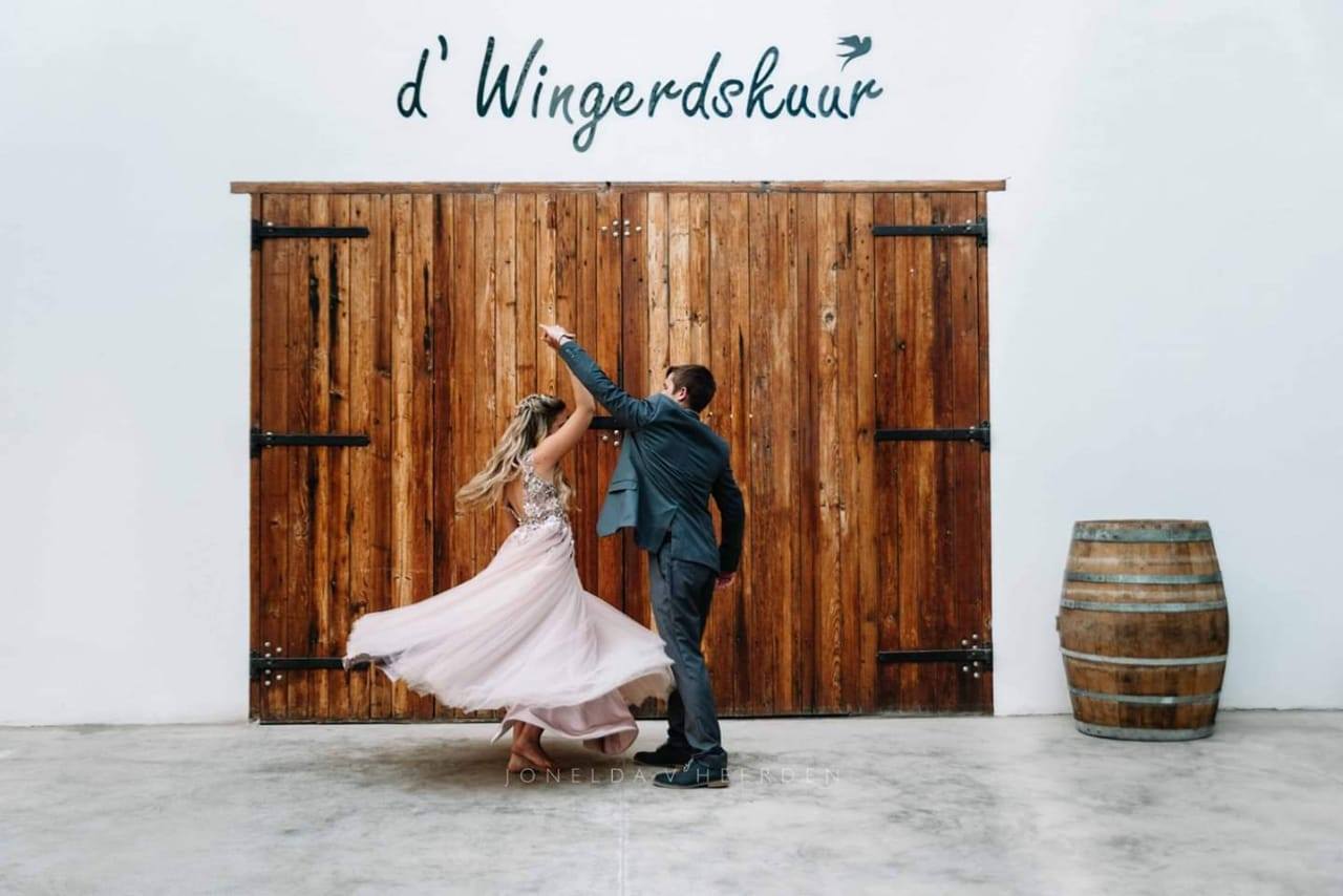 Couple dancing inside a rustic venue with wooden doors.
