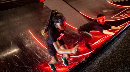 Two individuals climbing on the Warped Wall at Total Ninja.
