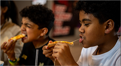 Two boys enjoying slices of pizza at Total Ninja