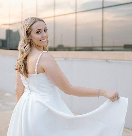 Bride in white gown with pearl details smiling at sunset
