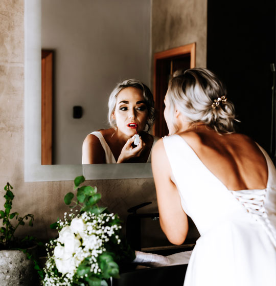 Bride applying lipstick in front of a mirror