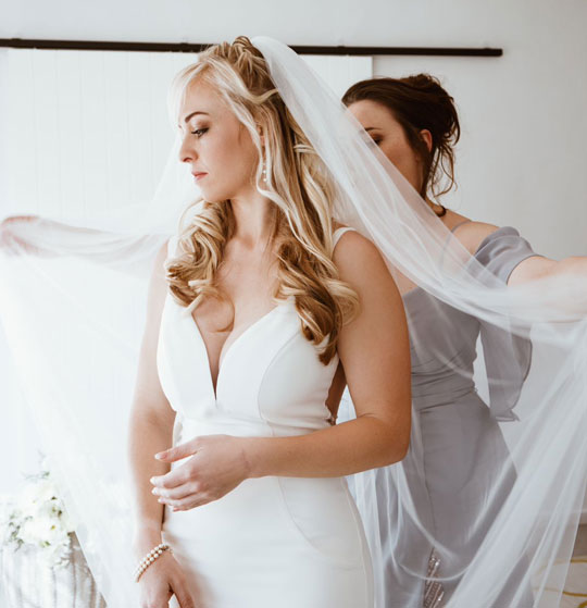 Bride in white gown being assisted with veil by bridesmaid