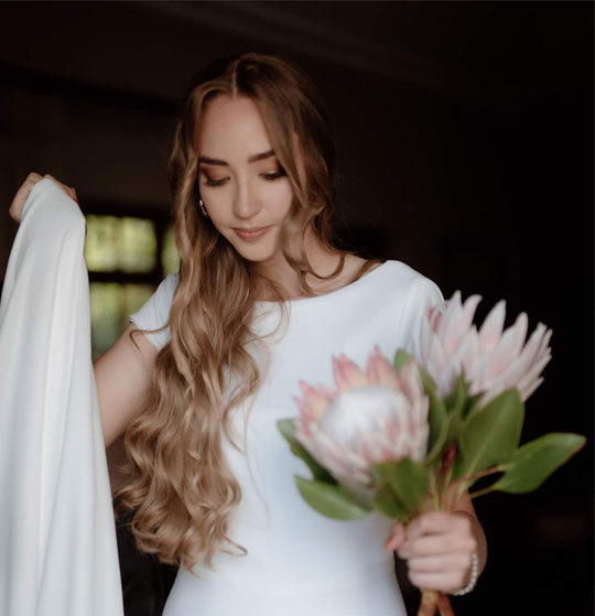Bride in white dress holding gown and bouquet
