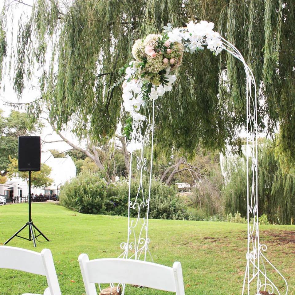 White ceremony arch with floral arrangement in a garden
