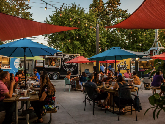 Outdoor scene with people dining at tables under umbrellas.