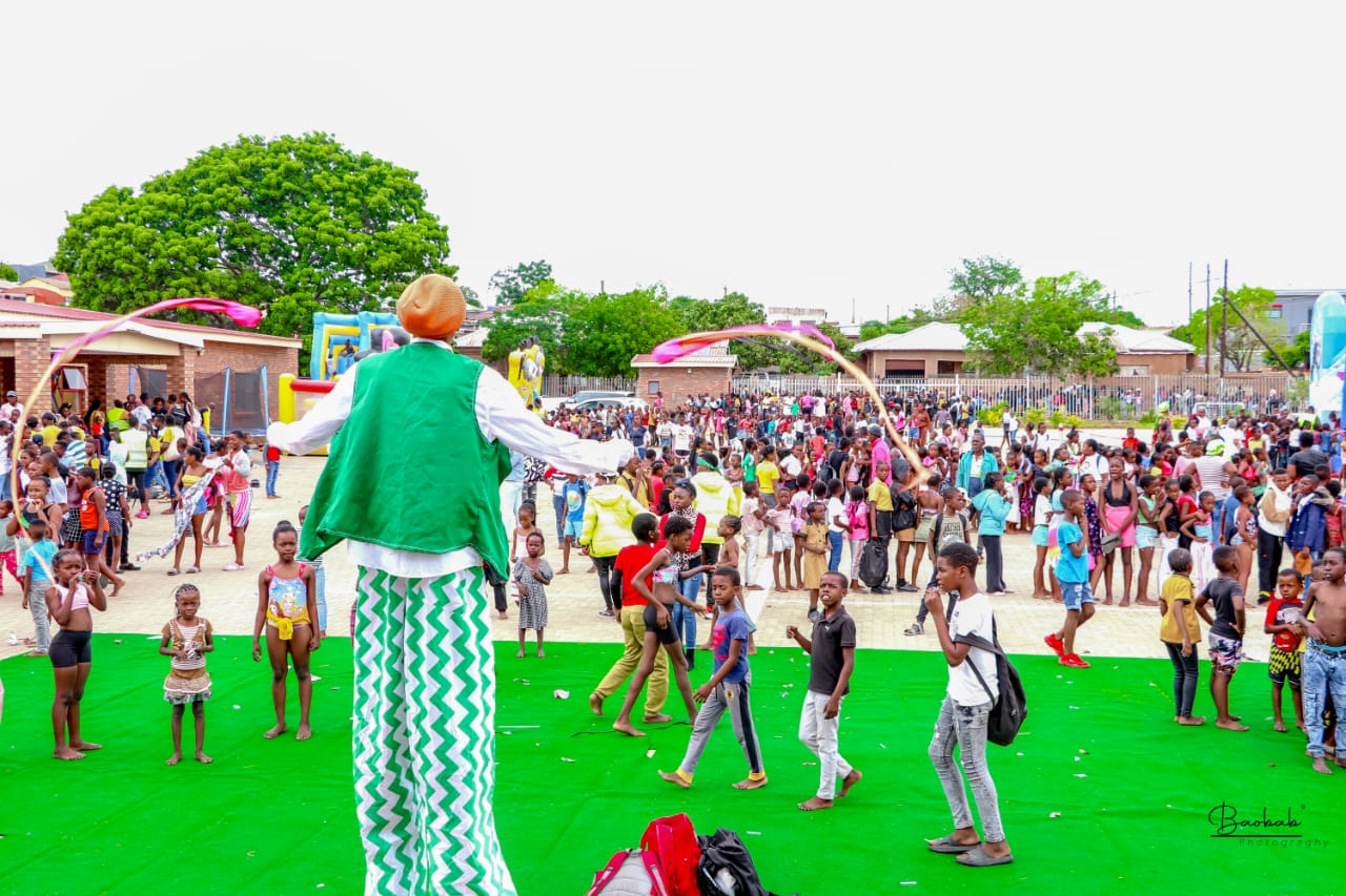 A stilt walker entertains a large crowd at a community event.