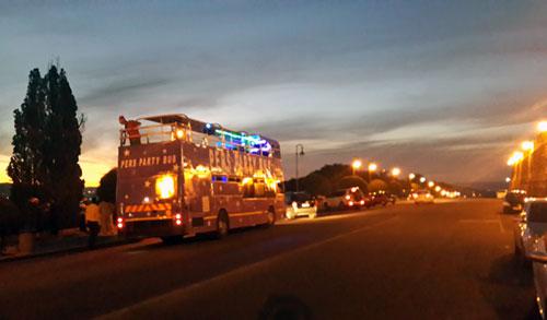 Pers Party Bus driving along a lit street at dusk.