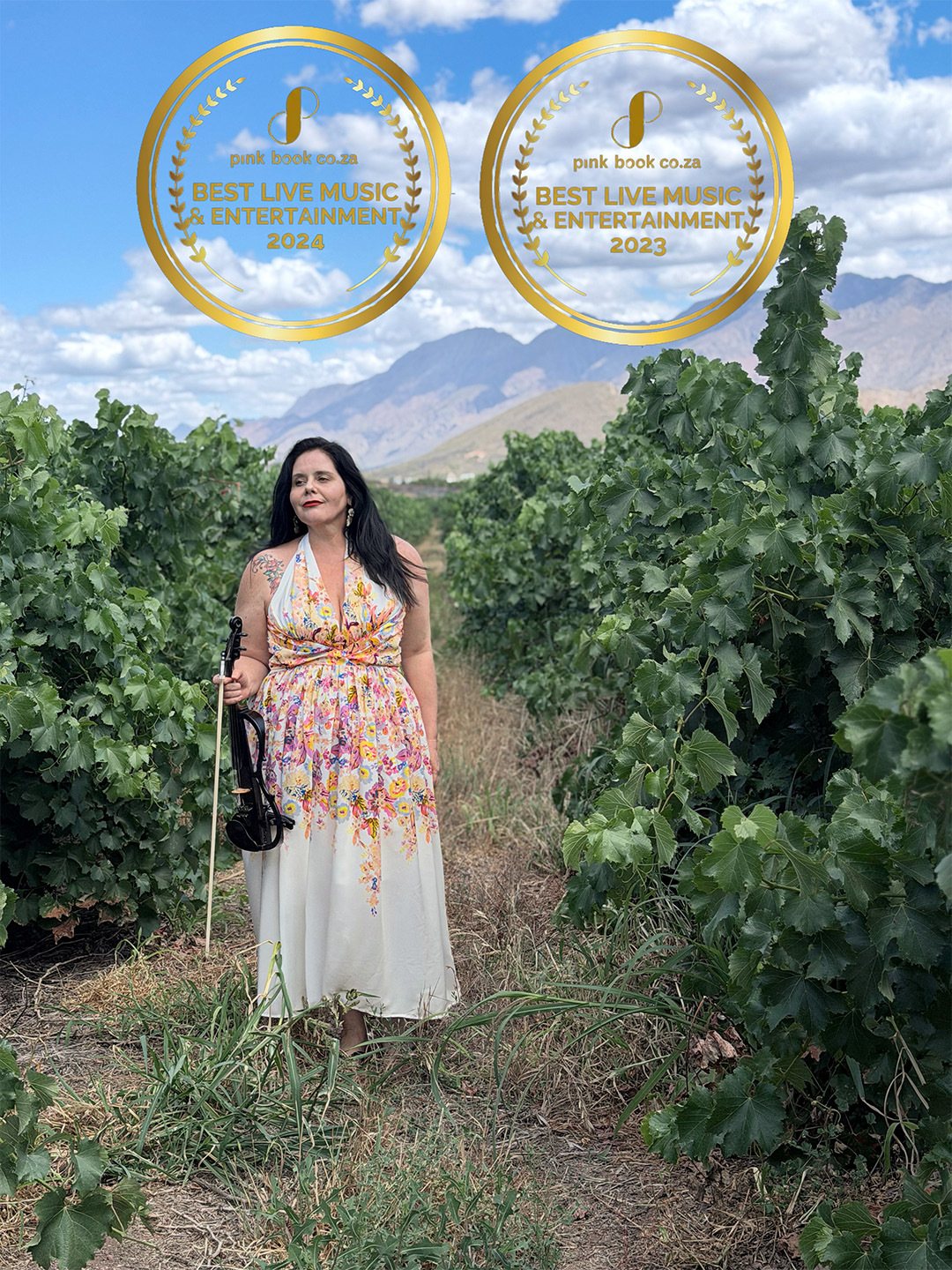 Violinist in floral dress standing in vineyard with awards.