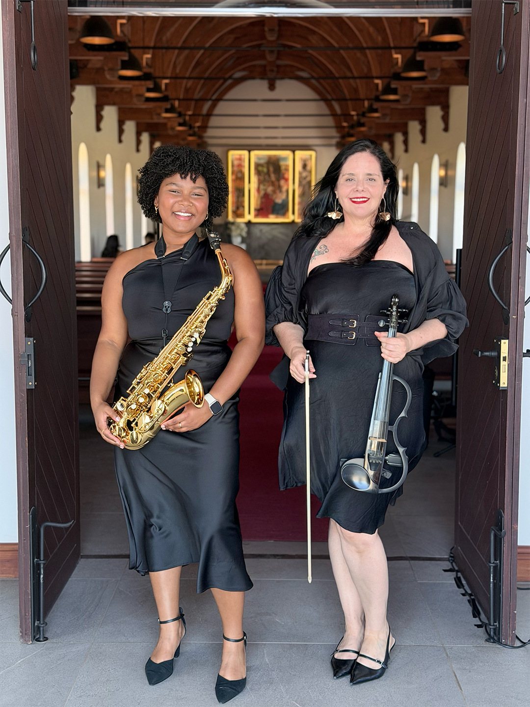 Two female musicians with a saxophone and violin at a church entrance