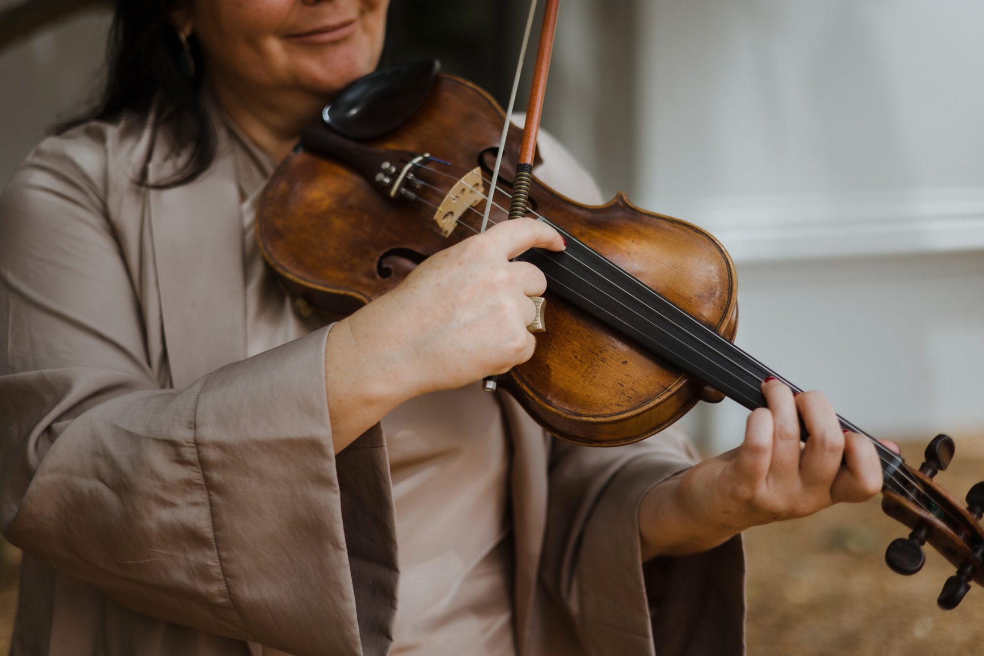 Musician in beige playing a wooden violin outdoors
