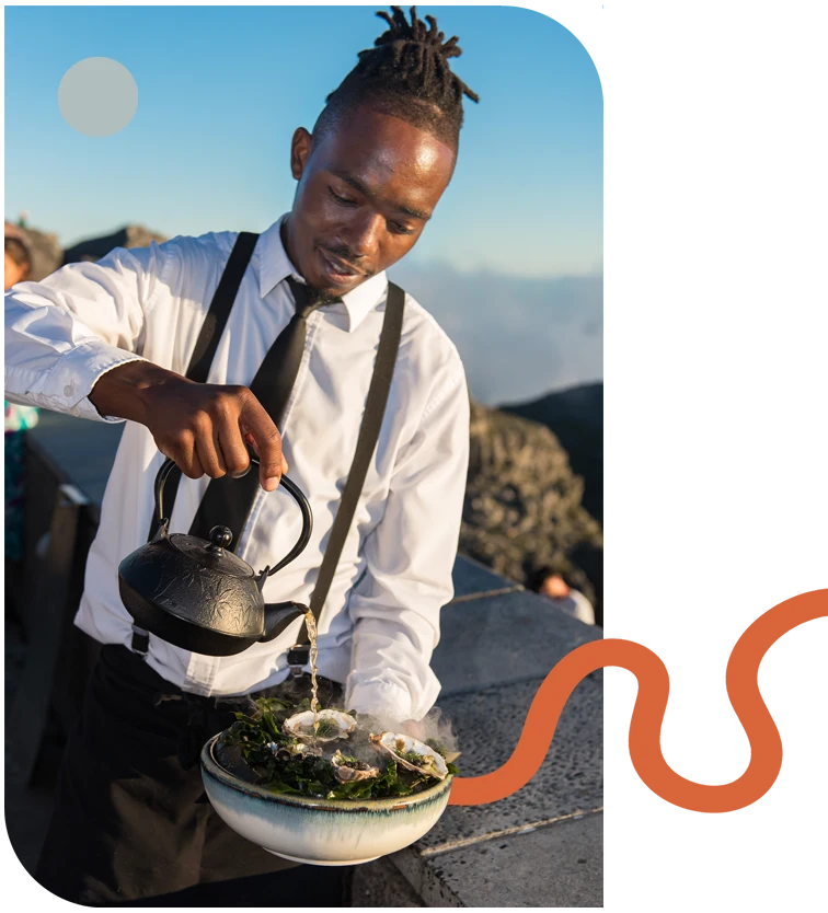 Staff member pouring tea over a dish with smoke effect.