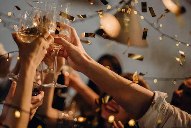 Hands raising glasses in a toast with confetti in the air